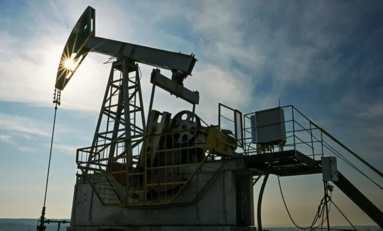 Silhouette of an oil pump against a bright sun and cloudy sky.