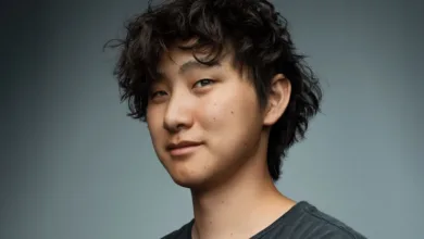 Close-up portrait of a young man with dark, curly hair, looking slightly off-camera with a subtle smile.