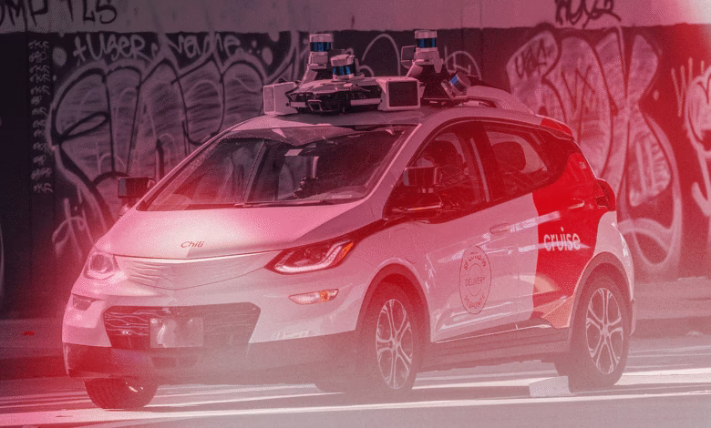 A white Cruise self-driving car with sensors on its roof drives past a graffiti-covered wall.