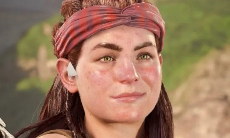 Close-up of Aloy, the protagonist from Horizon Forbidden West, smiling gently. She wears a red bandana and has freckles.