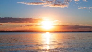 Sunset over calm water, with orange and pink clouds reflecting on the surface.
