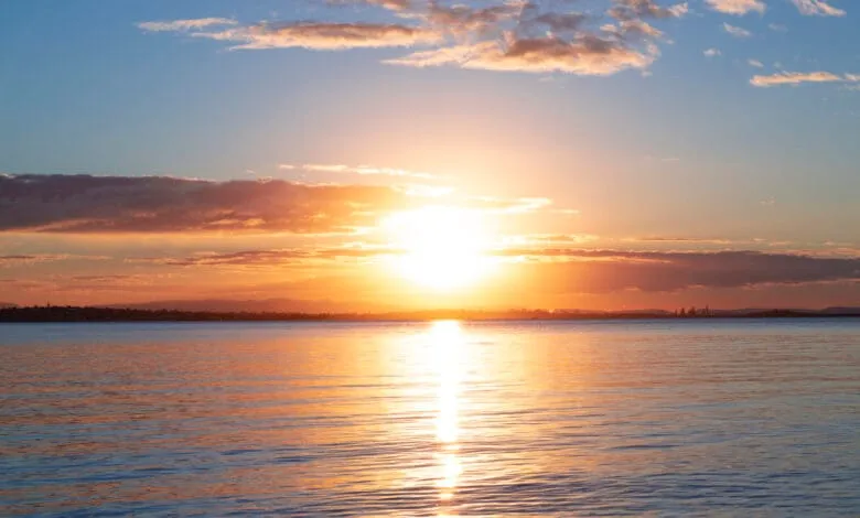 Sunset over calm water, with orange and pink clouds reflecting on the surface.