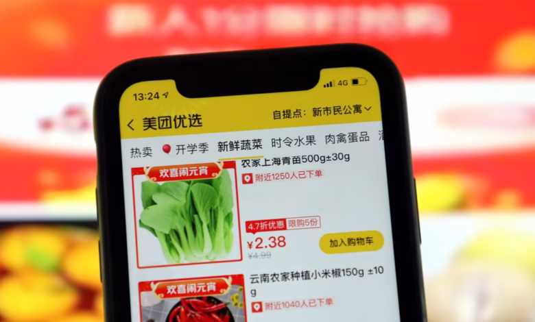 Close-up of a smartphone displaying a Chinese grocery app, showcasing bok choy and chili peppers for sale.