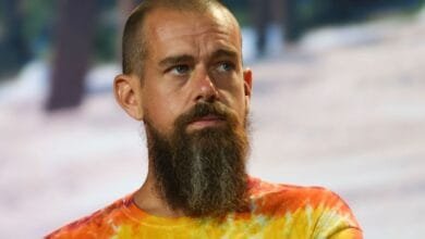 Close-up of Jack Dorsey, CEO of Twitter and Block, at a conference. He's wearing a tie-dye shirt and has a beard.