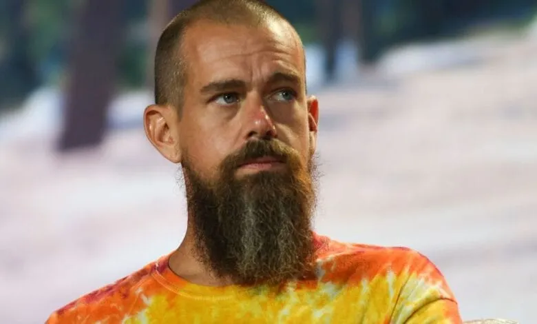 Close-up of Jack Dorsey, CEO of Twitter and Block, at a conference. He's wearing a tie-dye shirt and has a beard.