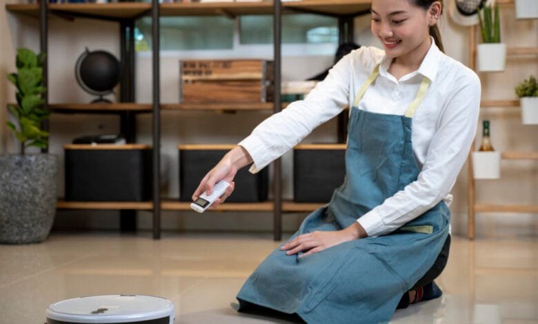 Woman in apron operates a robotic vacuum cleaner with a remote control in a modern home.