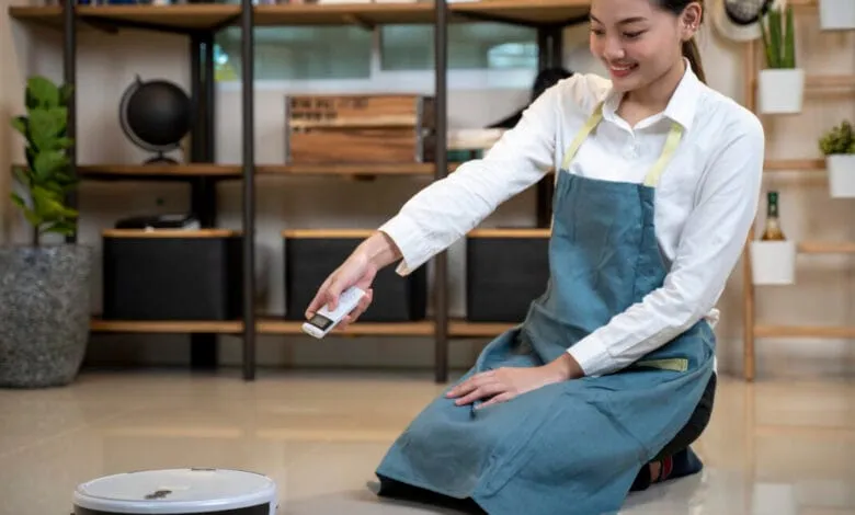 Woman in apron operates a robotic vacuum cleaner with a remote control in a modern home.