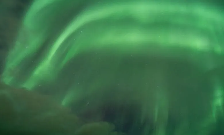 Vibrant green Northern Lights illuminate the night sky, creating a mesmerizing display of swirling light and color.