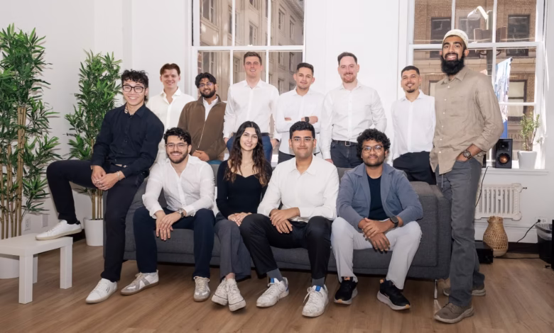 A diverse group of young professionals smiles for a photo, sitting and standing on a gray couch in a bright, modern office.