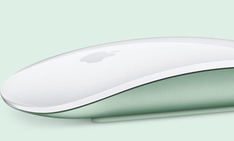 Close-up of a sleek, white Apple Magic Mouse with a pale green underside, set against a matching background.