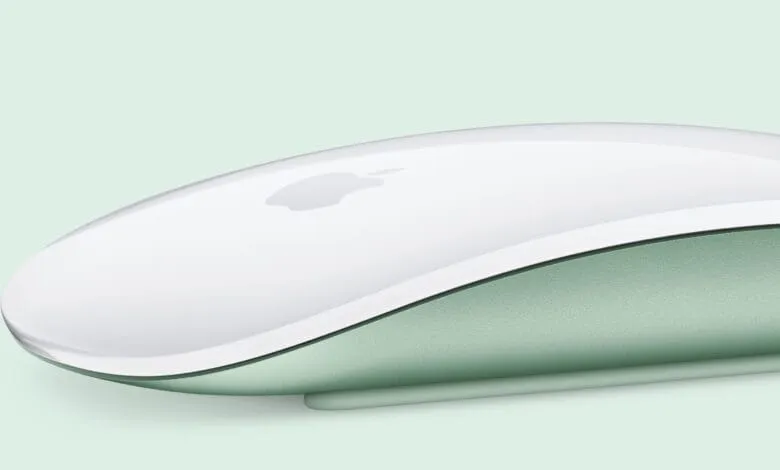 Close-up of a sleek, white Apple Magic Mouse with a pale green underside, set against a matching background.