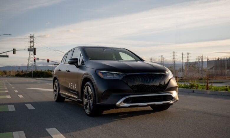 A dark gray Aeva SUV drives on a road at sunset, with power lines in the background.