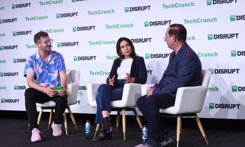 Three people sit on stage at TechCrunch Disrupt, engaged in conversation. The background features the TechCrunch Disrupt logo.