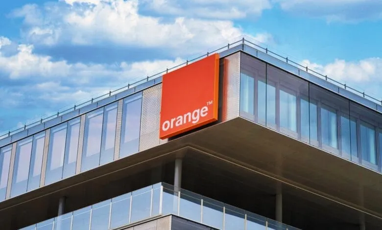 Orange telecommunications company logo on a modern glass building against a blue sky.