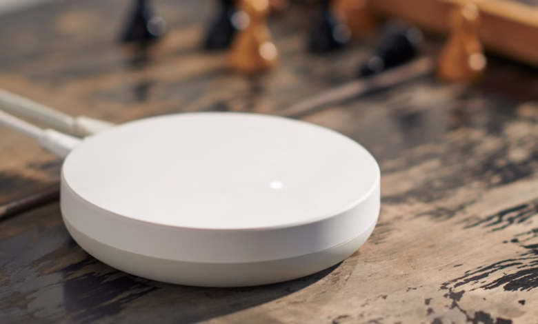 A white, round router sits on a rustic wooden table, with a blurred chessboard in the background.