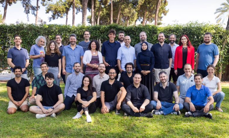 A diverse group of 30 people smiles for a group photo on a grassy lawn, trees and hedges in the background.