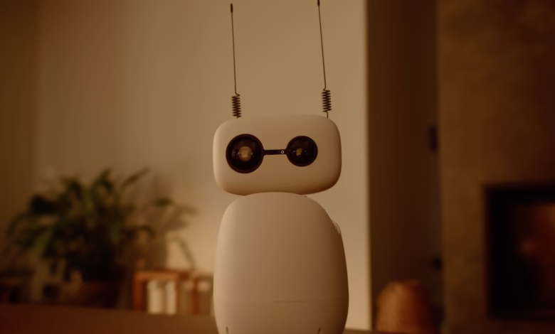 A small, white robot with antennae sits on a wooden table in a dimly lit room.