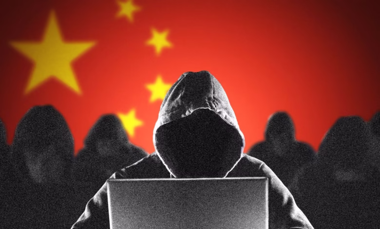Silhouetted figure in a hoodie uses a laptop against a blurred Chinese flag backdrop, suggesting cybercrime or hacking.