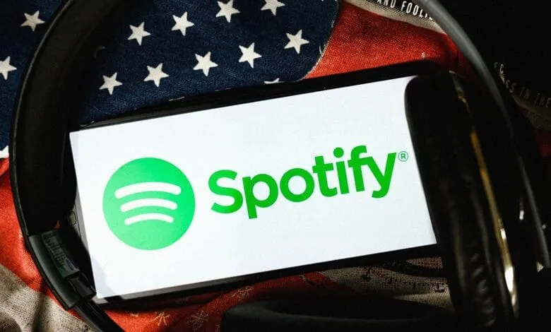 Spotify logo displayed on a phone screen, resting on an American flag with headphones.
