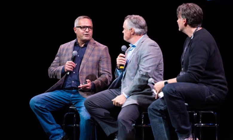 Three men sit on stools during a panel discussion, holding microphones and engaging in conversation.