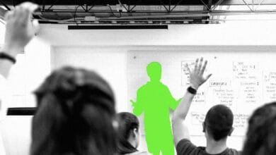 Presenter in lime green gives a presentation to a grayscale audience with hands raised, whiteboard shows database design.