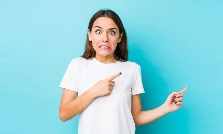 Woman in white t-shirt points to both sides with a surprised expression against a light blue background.