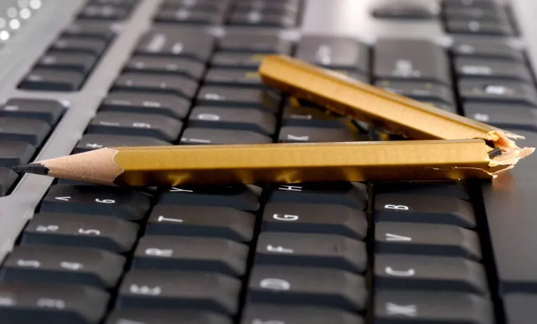 Two broken gold pencils lie on a black computer keyboard, symbolizing writer's block or technological frustration.