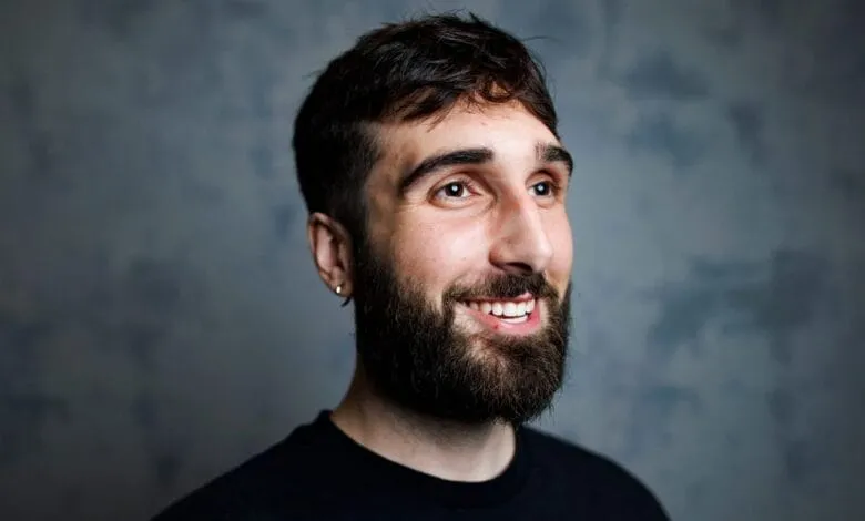 Smiling man with beard looks upward against a textured gray background.