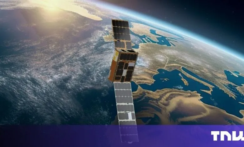 A satellite in Earth's orbit, solar panels deployed, against a backdrop of land and ocean. Sunlight glints off the water.