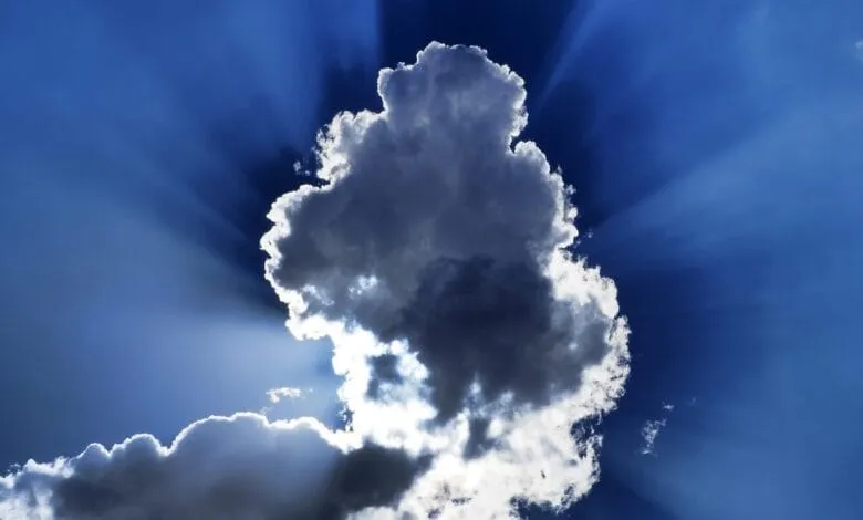 Dramatic sunbeams burst through a large cumulus cloud in a vibrant blue sky.
