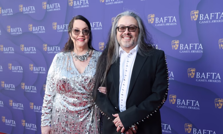 A couple poses at the BAFTA Games Awards. She wears a silver sequined dress; he's in a black jacket with studded sleeves.