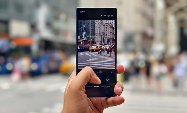 Hand holding smartphone displaying a NYC street scene with yellow cabs and pedestrians crossing.
