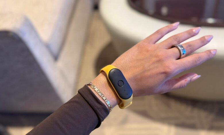 A person's wrist wearing a yellow fitness tracker with a black screen. The hand is slightly open, and a silver ring is visible.