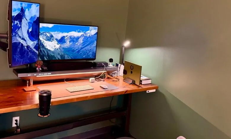 Modern home office setup with dual monitors displaying mountain vistas, a wooden desk, and a MacBook.