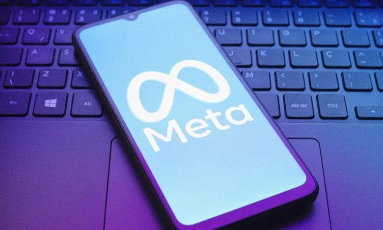 Smartphone displaying the Meta logo on a laptop keyboard. The screen is light blue with a white infinity symbol and the word 'Meta'.