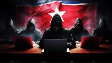 Anonymous figures in hoodies use laptops against a backdrop of the North Korean flag, suggesting cybercrime.