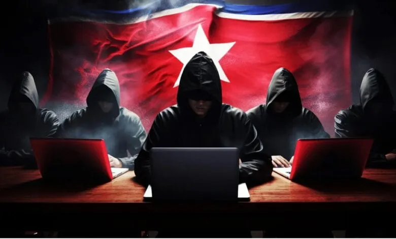 Anonymous figures in hoodies use laptops against a backdrop of the North Korean flag, suggesting cybercrime.