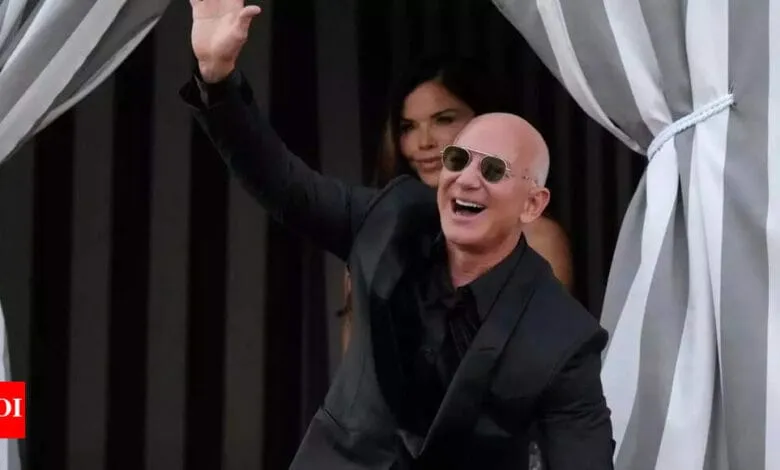 Jeff Bezos, Amazon founder, waves and smiles while wearing sunglasses and a black suit.