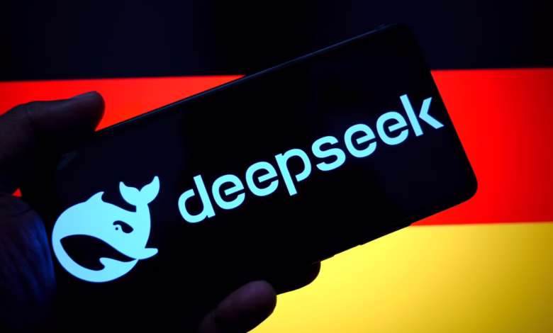 A hand holds a smartphone displaying the DeepSeek logo, a stylized whale, against a blurred German flag background.