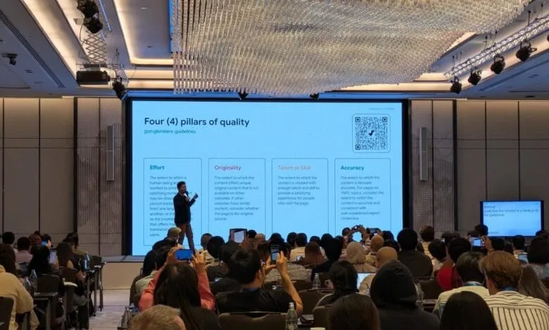 Speaker presents on four pillars of quality (Effort, Originality, Talent/Skill, Accuracy) at a conference; large audience listens attentively.