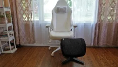 White Secretlab gaming chair with gray headrest and black footrest sits in front of a window with sheer curtains.