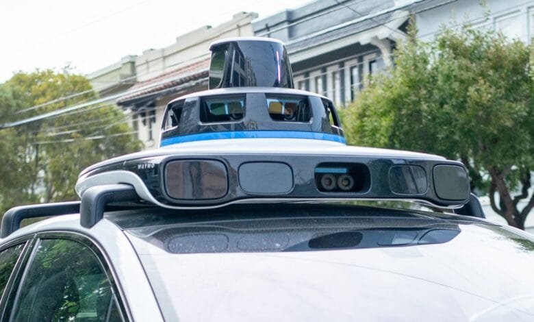 Close-up of a Waymo self-driving car's roof-mounted sensor array. The sensors are black and gray with a blue stripe.