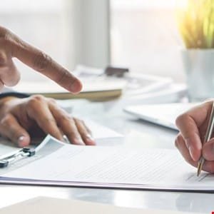 Close-up of hands signing a document, one hand pointing to the document.