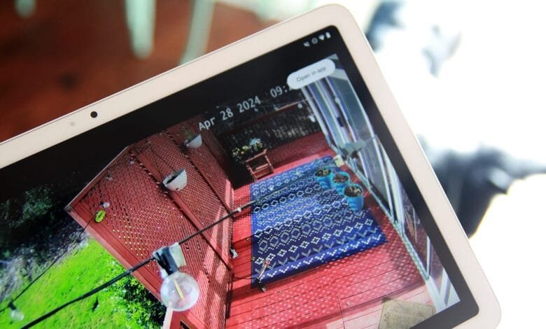 Tablet displaying a security camera feed of a red deck with a blue rug, potted plants, and a red lattice fence. The time stamp shows April 28, 2024.