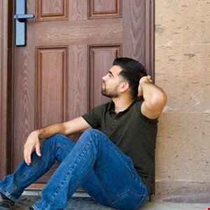 Man sits pensively on doorstep, hand in hair, looking away.