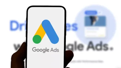 Close-up of a smartphone displaying the Google Ads logo. The background shows blurred text mentioning Google Ads.