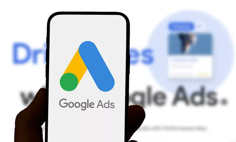 Close-up of a smartphone displaying the Google Ads logo. The background shows blurred text mentioning Google Ads.