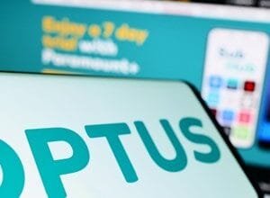 Close-up of the Optus logo displayed on a smartphone screen, with a blurred Optus website in the background.