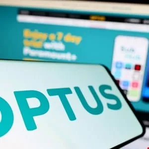Close-up of the Optus logo displayed on a smartphone screen, with a blurred Optus website in the background.