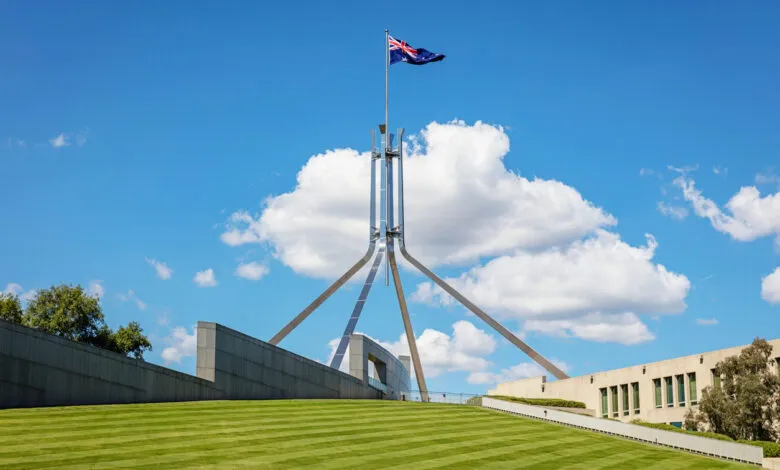 Australian Parliament House in Canberra with the Australian flag flying high against a blue sky.